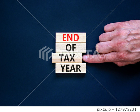 End of tax year symbol. Concept words phrase End of tax year on beautiful wooden blocks. Beautiful black paper background. Businessman's hand. Business End of tax year concept. Copy space. 127975231
