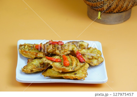 A plate of Indonesian fried vegetable snacks or bakwan topped with red chilies, set against an orange background. A plate of Indonesian fried vegetable snacks or bakwan topped with red chilies, set against an orange background. 127975457