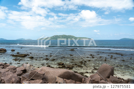 View of granite coastal rocks and ocean waves with distant islands on the horizon under cloudy View of granite coastal rocks and ocean waves with distant islands on the horizon under cloudy 127975581