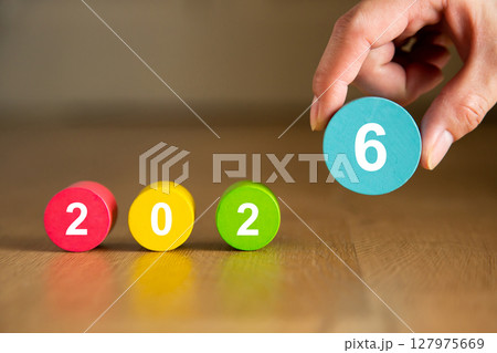 Hand placing the number six to complete the year 2026 with colorful wooden cylinders 127975669