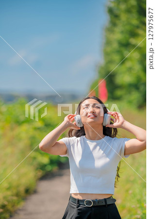 青空のもとでヘッドホンで音楽を聴いている白いTシャツの若い女性 127975677