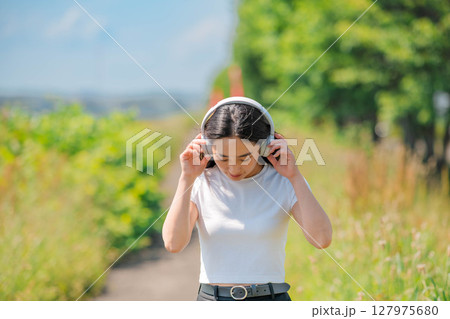 青空のもとでヘッドホンで音楽を聴いている白いTシャツの若い女性 青空のもとでヘッドホンで音楽を聴いている白いTシャツの若い女性 127975680