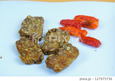Four pieces of fried tempeh, a traditional Indonesian soy based food, arranged with several red chilies on a white background. Four pieces of fried tempeh, a traditional Indonesian soy based food, arranged with several red chilies on a white background. 127975736