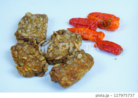 Four pieces of fried tempeh, a traditional Indonesian soy based food, arranged with several red chilies on a white background. 127975737