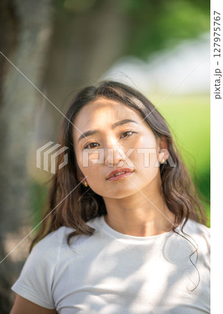 木漏れ日の中でリラックスする若い女性のポートレート 127975767