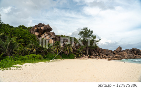 Granite cliffs rise above palm trees on the beach of La Digue island in Seychelles 127975806