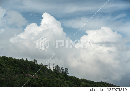 Towering cumulus clouds rise above tropical forest on La Digue island in Seychelles 127975819