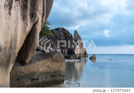 Granite rock formations rise above calm water on La Digue island, Seychelles 127975843