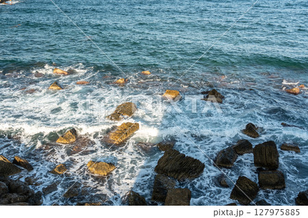 Waves crash against large rocks forming a dynamic marine pattern 127975885