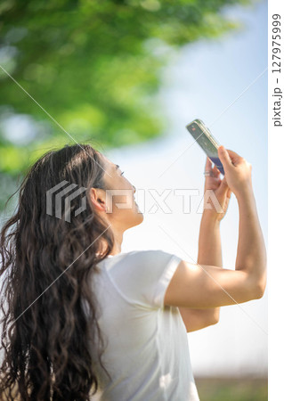 木漏れ日の中、スマホで撮影する若い女性 127975999
