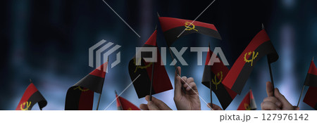 Angola flags in their hands on a blurred urban background 127976142