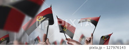 Angola flags in their hands on a blurred urban background 127976143