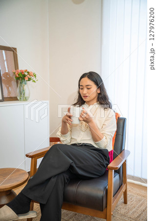 室内でリラックスをしながら飲み物を飲む若い女性 127976200