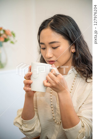 室内でリラックスをしながら飲み物を飲む若い女性 127976204