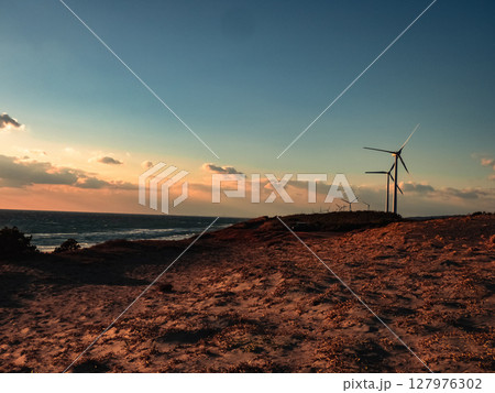 夕日に照らされる海と風力発電機 127976302