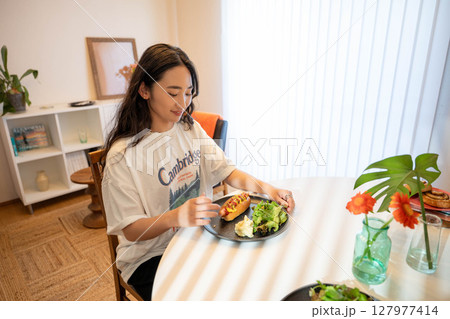 室内でカジュアルな格好をしながらご飯を食べる若い女性 室内でカジュアルな格好をしながらご飯を食べる若い女性 127977414