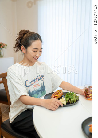 室内でカジュアルな格好をしながらご飯を食べる若い女性 127977415