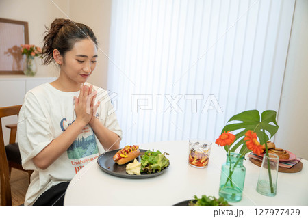 室内でカジュアルな格好をしながらご飯を食べる若い女性 室内でカジュアルな格好をしながらご飯を食べる若い女性 127977429