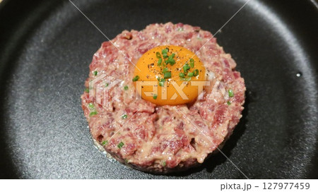close up of raw egg and tuna tartar in a round shape on a black plate 127977459