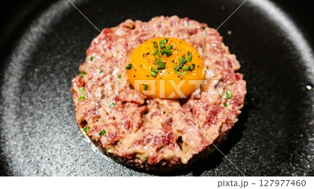 close up of raw egg and tuna tartar in a round shape on a black plate 127977460