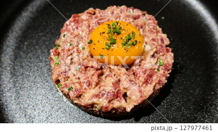 close up of raw egg and tuna tartar in a round shape on a black plate 127977461