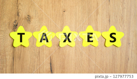 Taxes symbol. Concept word Taxes on beautiful yellow paper stars. Beautiful wooden table wooden background. Business lifestyle taxes concept. Copy space. Taxes symbol. Concept word Taxes on beautiful yellow paper stars. Beautiful wooden table wooden background. Business lifestyle taxes concept. Copy space. 127977753