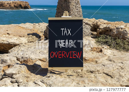 Tax year overview symbol. Concept words Tax year overview on beautiful black yellow blackboard. Beautiful stone and blue sea sky background. Business tax year overview concept. Copy space. 127977777
