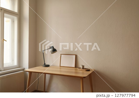 Minimalist workspace. Wooden desk, gray lamp, empty horizontal picture frame, poster mockup. Coffee cup on wooden tray by window. Modern Scandinavian interior, natural light. Home office setup. 127977794