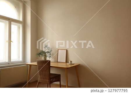 Vase with pine tree branches. Blank vertical wooden picture frame mockup. Home office table near window. Minimal Scandi boho interior. Cup of tea, coffee. Beige wall background. Christmas decor. 127977795