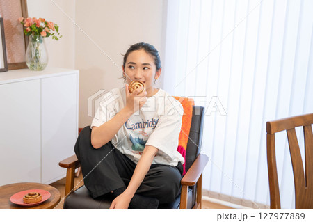 椅子に座ってパンを食べる若い女性 椅子に座ってパンを食べる若い女性 127977889