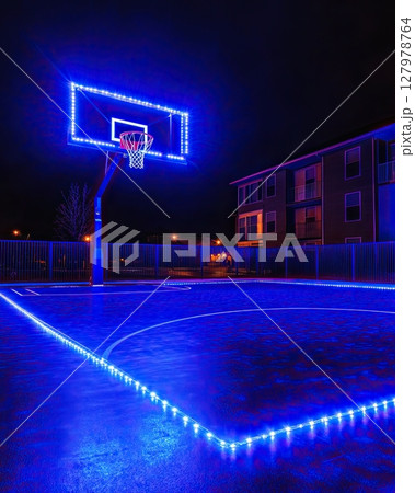 Dark basketball arena with glowing blue lighting and central hoop 127978764