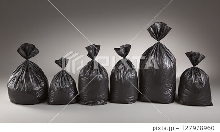 A row of sealed black plastic garbage bags stand side-by-side, increasing in size from left to right, against a gradient gray background. 127978960