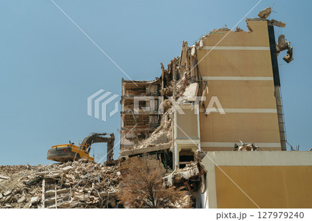 Demolition site with a collapsed building, exposed rebar, and a bulldozer Demolition site with a collapsed building, exposed rebar, and a bulldozer 127979240