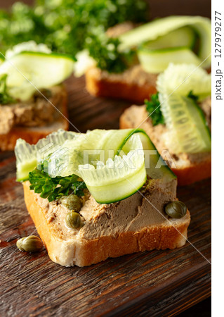 Open sandwiches with pate, cucumber, capers, and parsley on a old cutting board. 127979277
