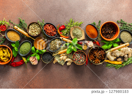 A stunning spread of fresh spices and herbs, meticulously arranged on a deep brown backdrop, capturing their vibrant colors and tantalizing aromas 127980183