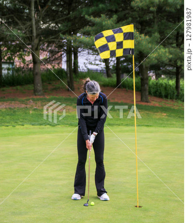 Woman Preparing to Putt on a Golf Course Surrounded by Trees 127981987