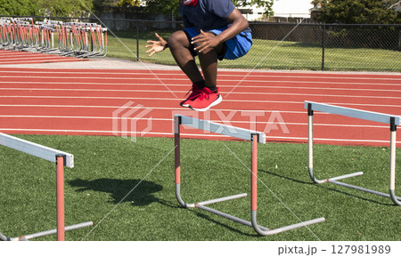 Athlete Jumps Over Hurdles on a Training Field 127981989