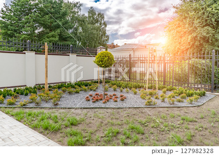 Back and front yard cottage garden, flowering plant and green grass lawn, brown pavement and orange brick wall, evergreen trees on background, in good care maintenance landscaping in park Back and front yard cottage garden, flowering plant and green grass lawn, brown pavement and orange brick wall, evergreen trees on background, in good care maintenance landscaping in park 127982328
