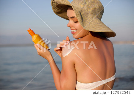 Beautiful Woman Face Portrait. Beauty Skin Care Concept. Young Woman Applying Suntan Lotion on Face. Sunscreen Solar Cream. Sun protection. The Girl Uses Moisturizer Sunblock Beauty Skin Care Concept. 127982542