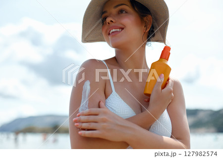 A young woman applying sun cream or sunscreen on her tanned shoulder to protect her skin from the sun. Skin and Body Care Concept 127982574