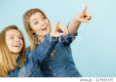 Two happy women friends wearing jeans outfit poitning 127983335