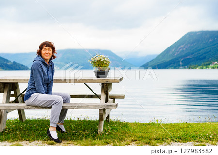 Woman tourist relax on fjord shore, Norway Woman tourist relax on fjord shore, Norway 127983382