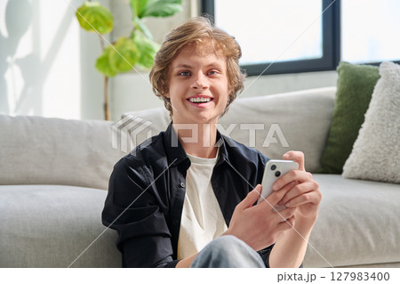 Portrait of happy handsome teenager guy with smartphone at home 127983400