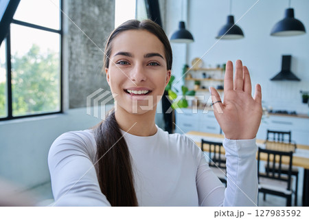 Close-up selfie portrait of teenage female looking waving hand at web camera Close-up selfie portrait of teenage female looking waving hand at web camera 127983592