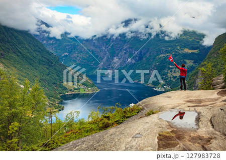 Tourist over Geirangerfjord holds norwegian flag Tourist over Geirangerfjord holds norwegian flag 127983728