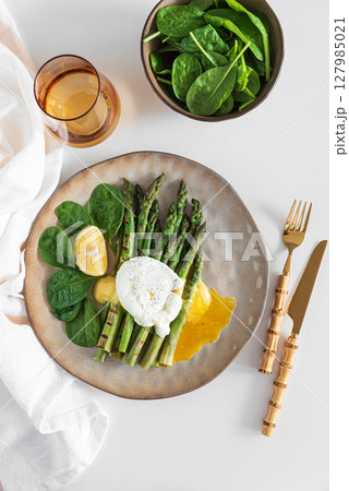 Poached egg with grilled asparagus, spinach, and hollandaise sauce on white table. Top view 127985021