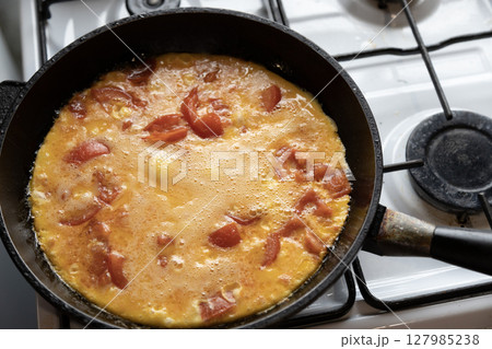 scrambled eggs with tomatoes in a frying pan on a gas stove 127985238