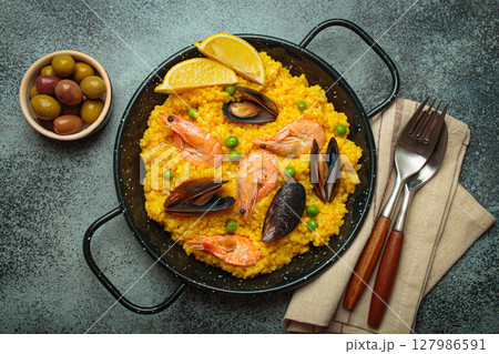 Spanish seafood Paella with shrimps, mussels, peas and lemon in a pan on dark rustic background top view 127986591