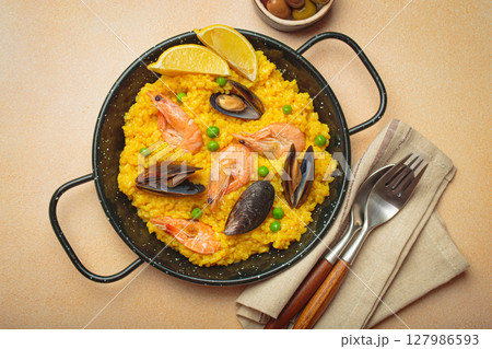 Spanish seafood Paella with shrimps, mussels, peas and lemon in a pan on light beige background top view 127986593