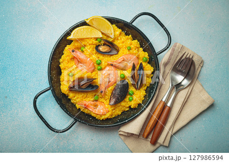 Spanish seafood Paella with shrimps, mussels, peas and lemon in a pan on light blue background top view. Mediterranean meal 127986594